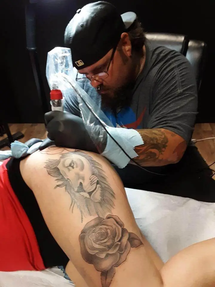 Brandon Williams tattooing a lion and rose design at Till Death Tattoo Studio